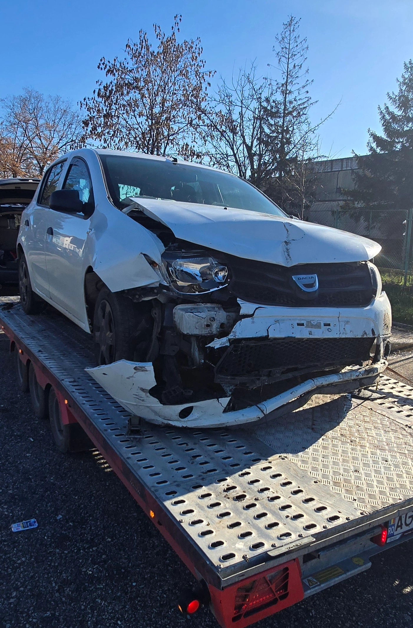 Dacia albă avariată transportată pe platformă